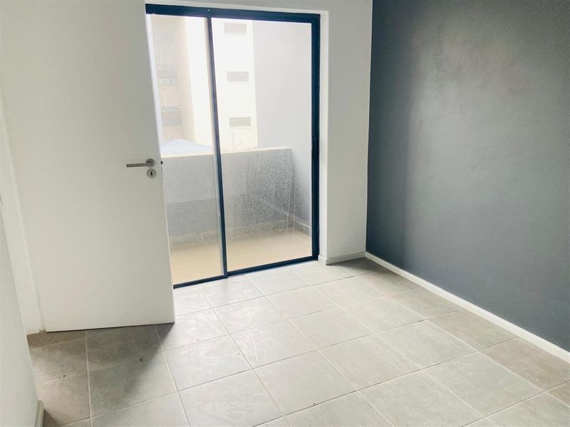 An empty bedroom featuring neutral tiled flooring, a dark grey accent wall, and a sliding glass door providing access to a balcony.