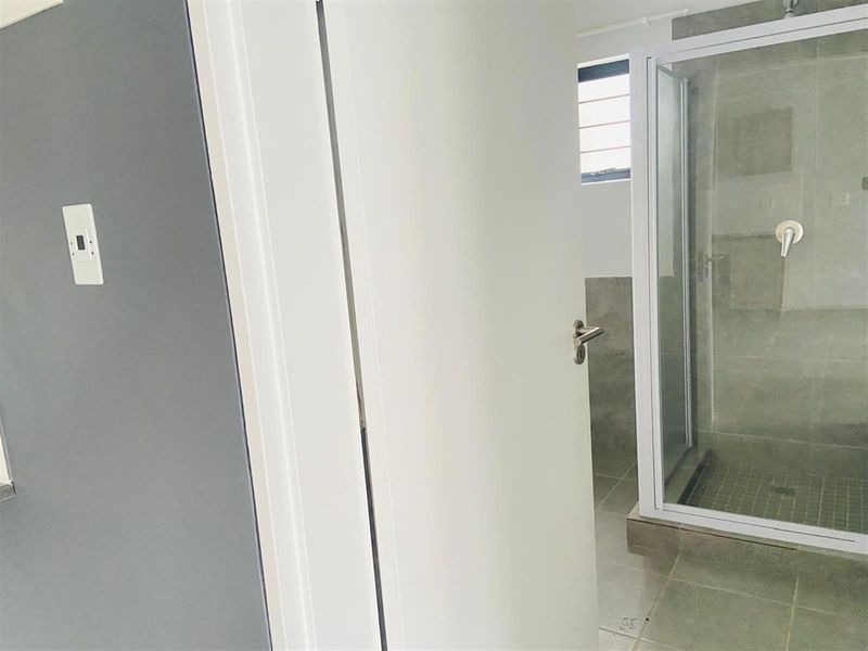 A clean, modern bathroom featuring a glass-enclosed shower with neutral grey tiling and contemporary fixtures.