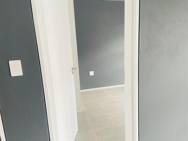 A view through a doorway into an empty bedroom featuring neutral grey walls and light-colored tiled flooring.