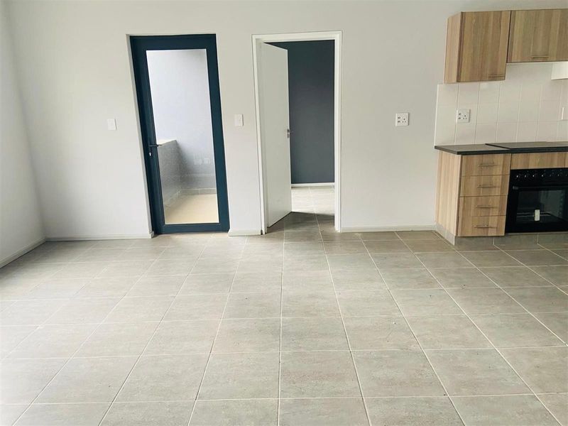 An open-plan living and kitchen area featuring neutral tiled flooring, modern cabinetry, and direct access to an outdoor balcony space.