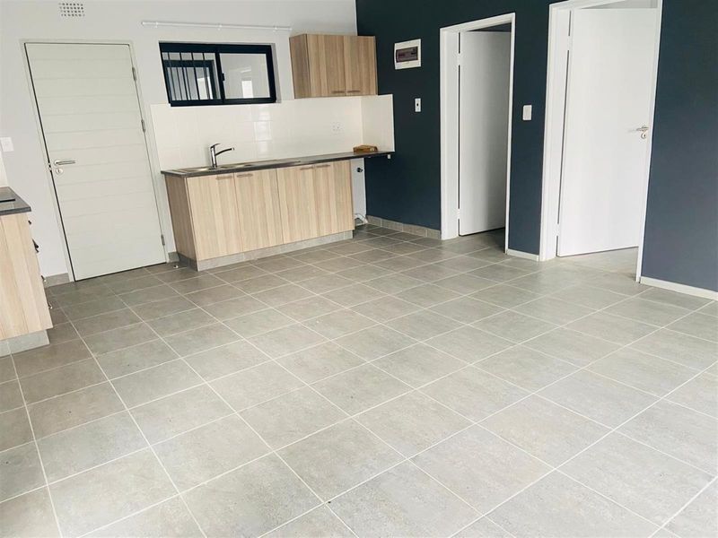 An open-plan living area featuring tiled flooring, a compact kitchen with light wood cabinetry, and access to adjacent rooms.