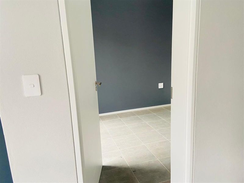 A view through a doorway into an empty bedroom featuring neutral tiled flooring and a dark grey accent wall.