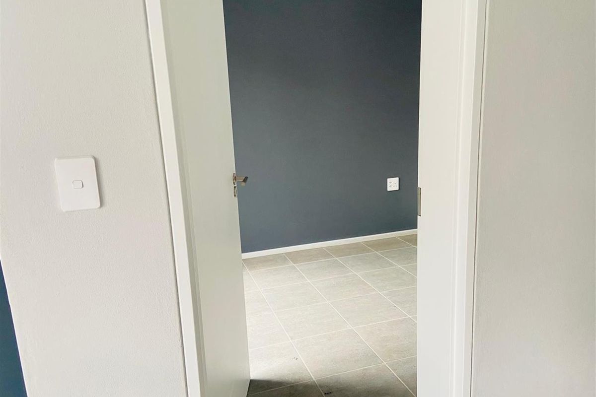 A view through a doorway into an empty bedroom featuring neutral tiled flooring and a dark grey accent wall.