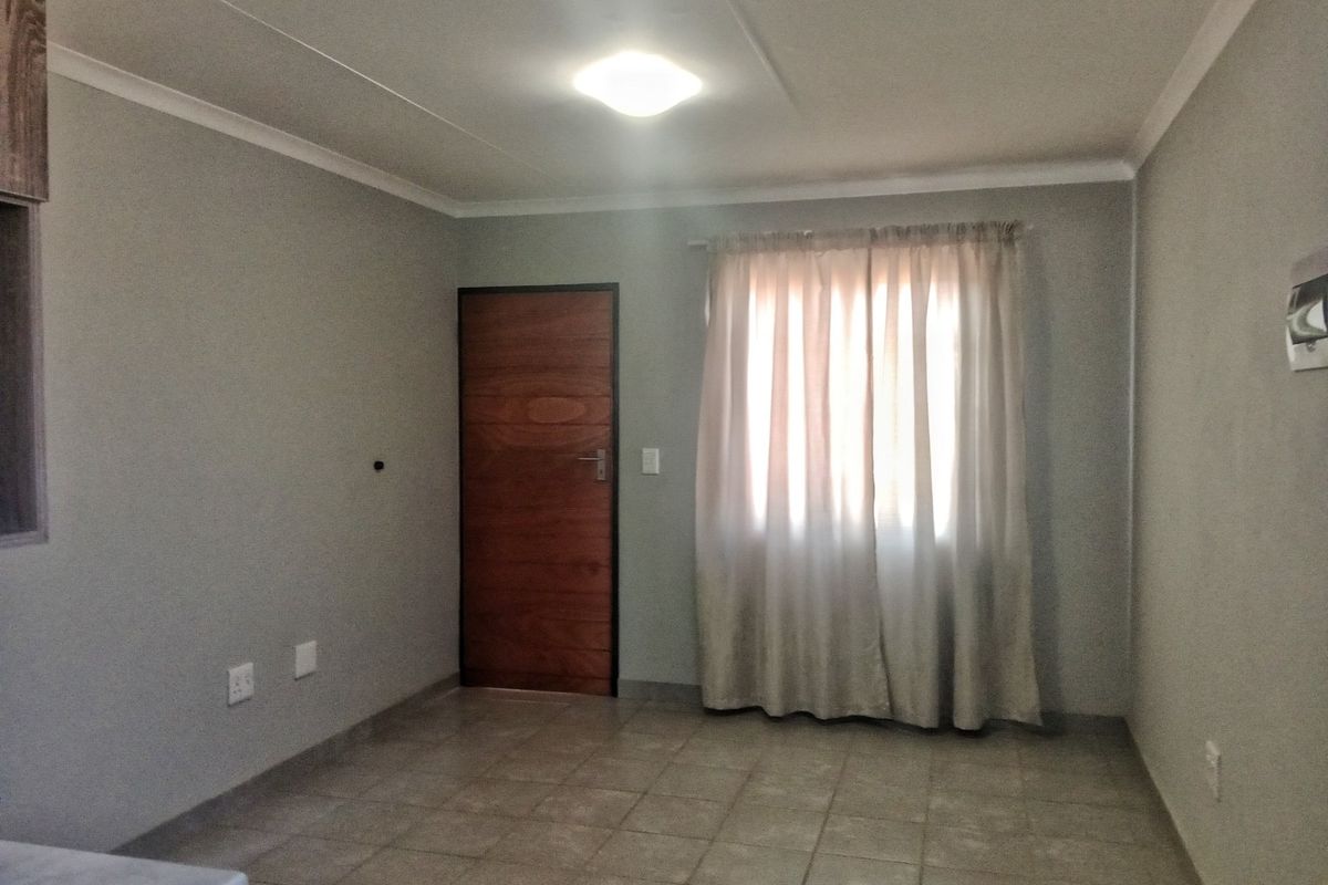 An empty living area featuring neutral grey walls, tiled flooring, and a wooden door, providing a clean and versatile space for customization.