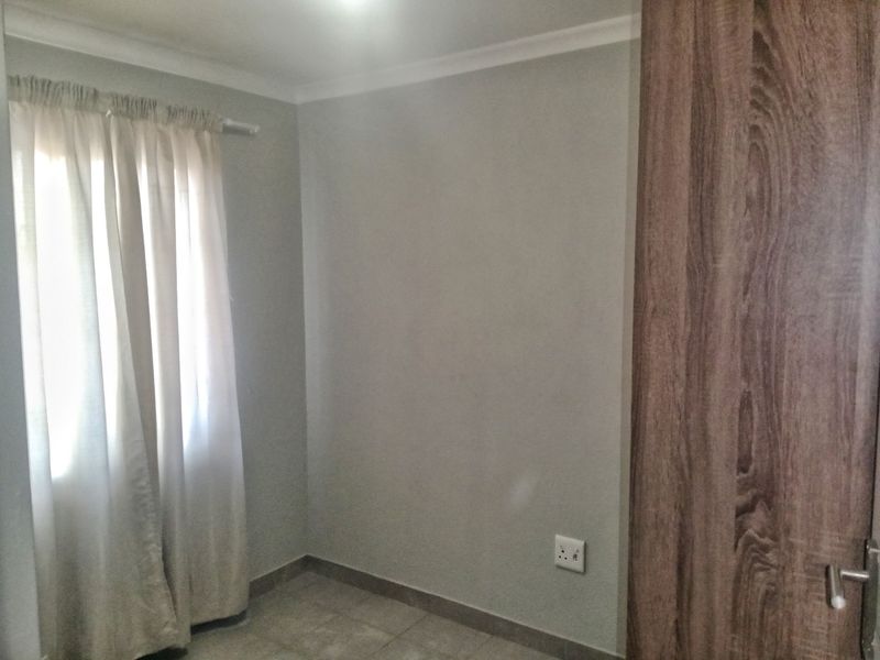 A clean, empty bedroom featuring neutral wall paint, tiled flooring, and a built-in wooden cupboard.