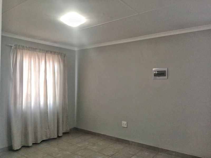 A clean, empty bedroom featuring neutral grey walls, tiled flooring, and a flush-mount ceiling light, providing a versatile space ready for personalization.