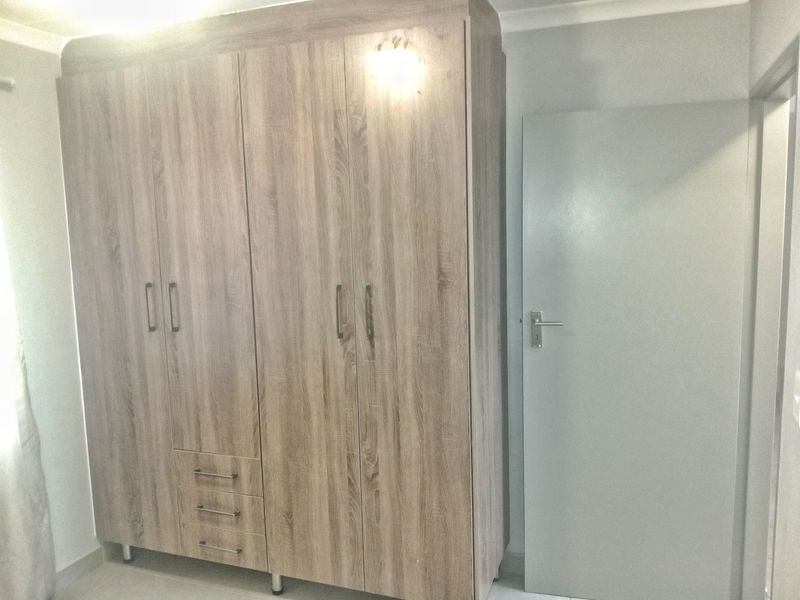 A bedroom interior featuring a large, modern wood-finish built-in wardrobe and a standard internal door.