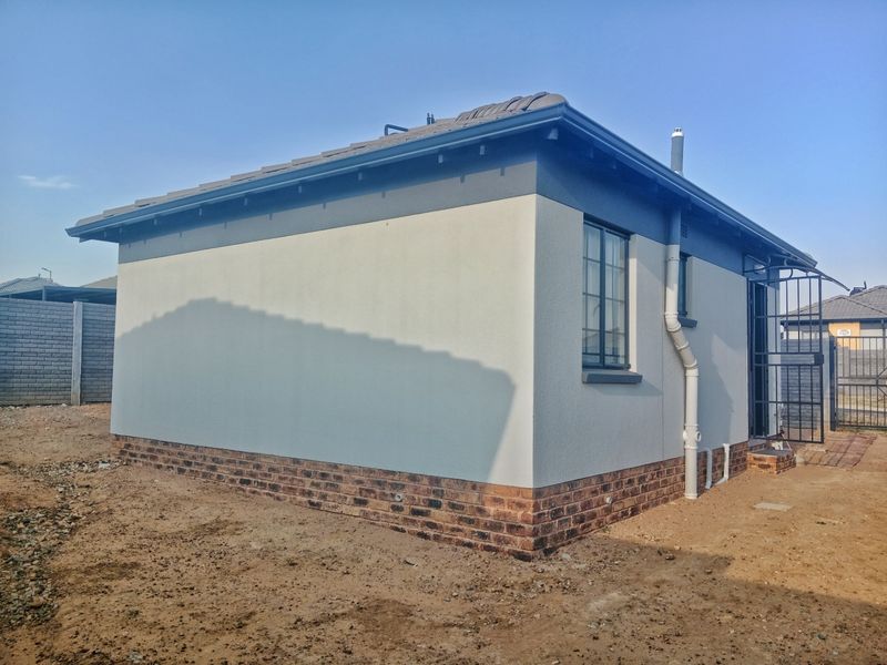 A view of the rear exterior elevation featuring a clean rendered finish, brick base, and secure entrance gate.