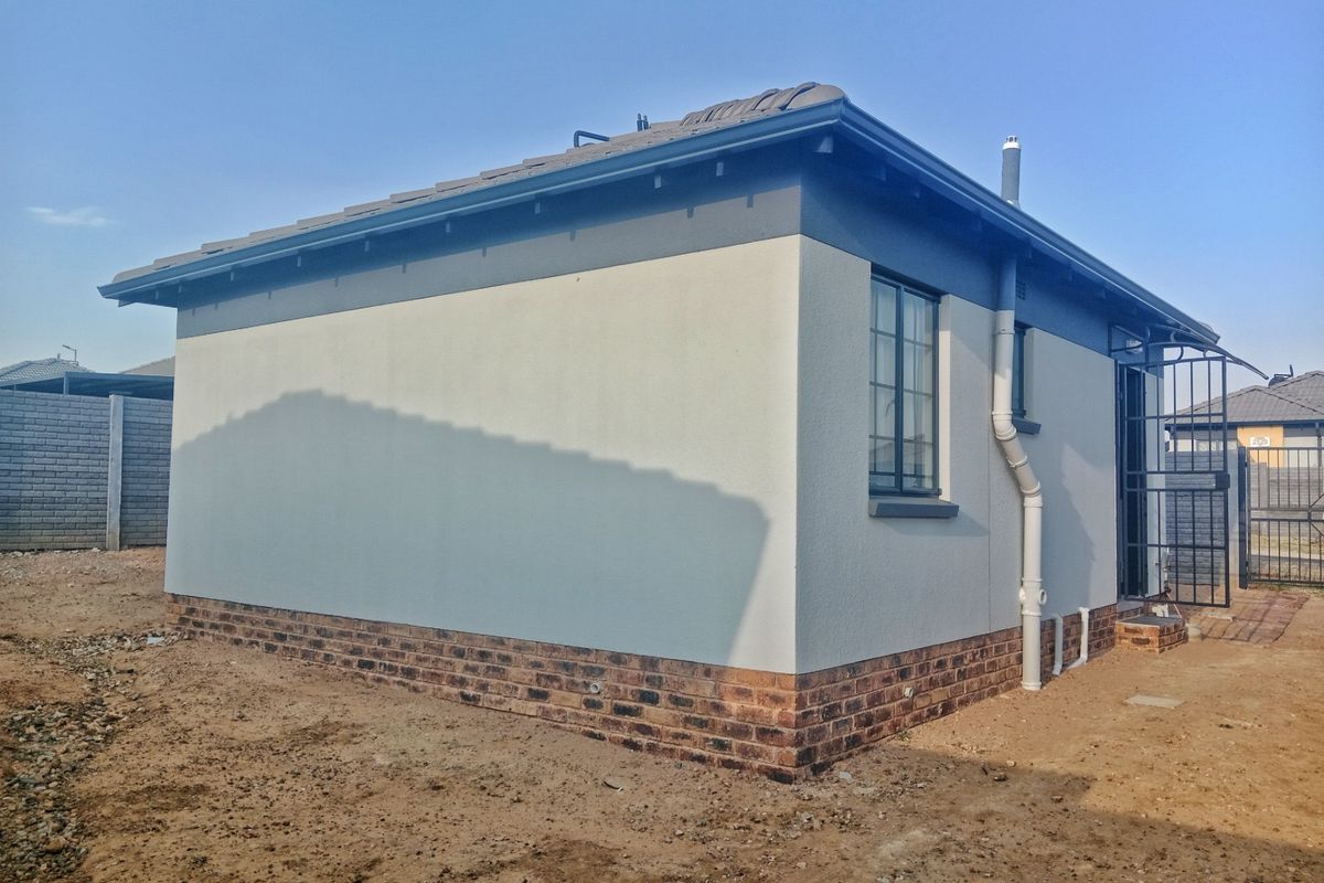 A view of the rear exterior elevation featuring a clean rendered finish, brick base, and secure entrance gate.