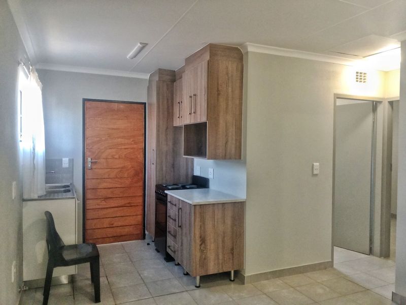 A compact kitchen featuring modern wood-look cabinetry, laminate countertops, a stainless steel sink, and tiled flooring, providing a functional and clean preparation space.