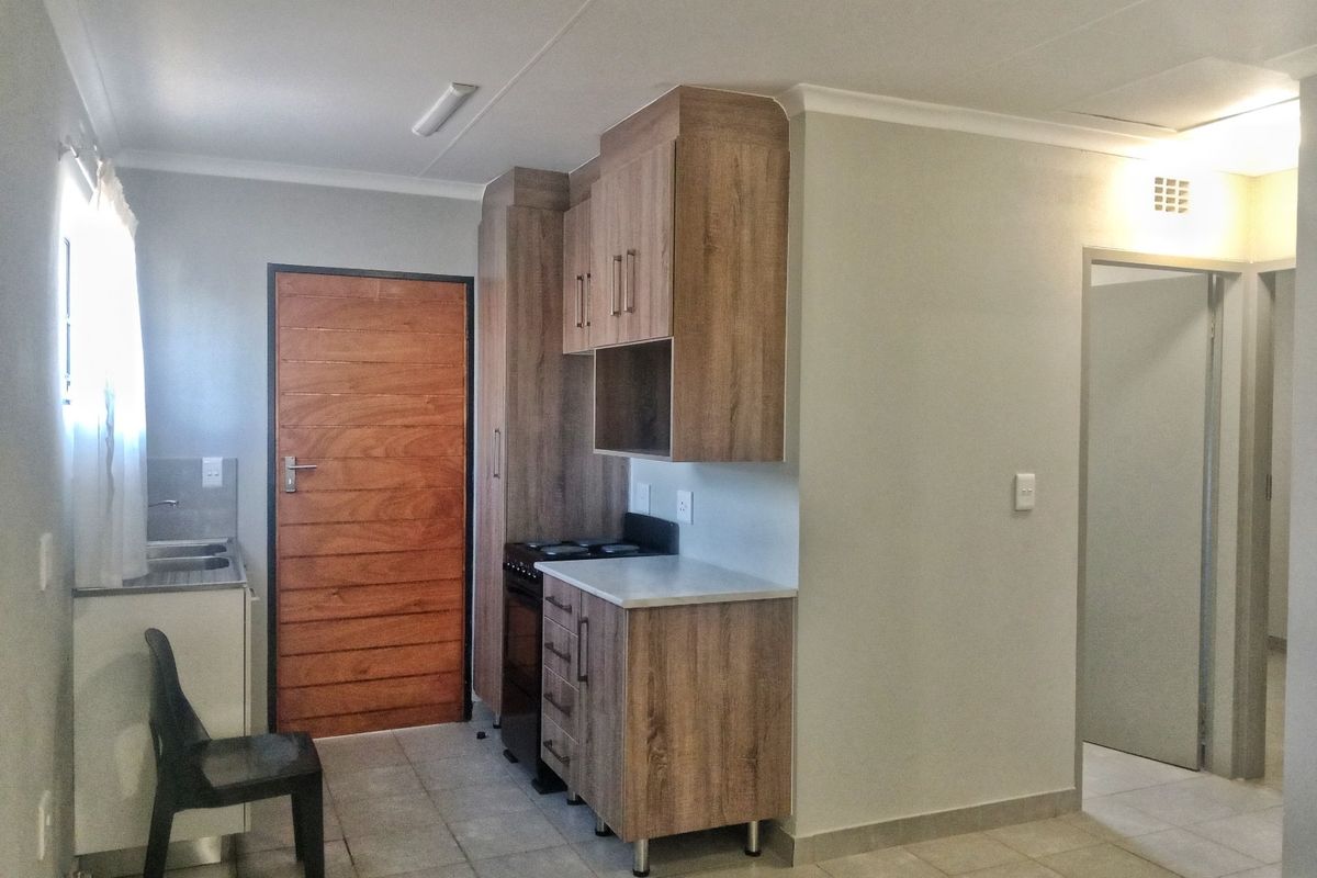A compact kitchen featuring modern wood-look cabinetry, laminate countertops, a stainless steel sink, and tiled flooring, providing a functional and clean preparation space.