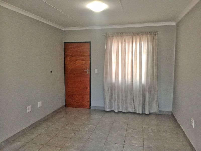 A clean, empty bedroom featuring neutral grey walls, tiled flooring, and a wooden door, providing a versatile space ready for personalization.