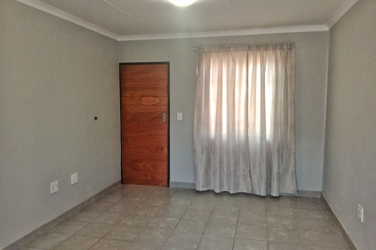 A clean, empty bedroom featuring neutral grey walls, tiled flooring, and a wooden door, providing a versatile space ready for personalization.