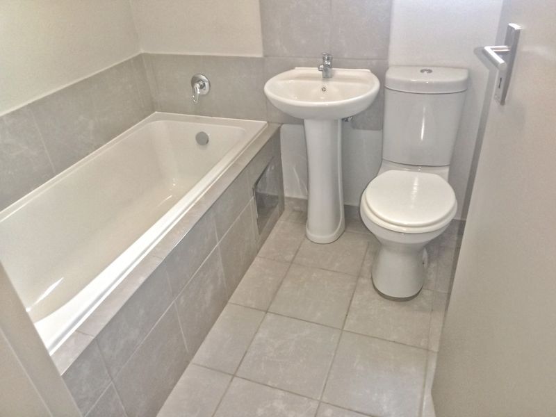 A clean and functional bathroom featuring a bathtub, pedestal basin, and toilet with neutral-toned wall and floor tiling.