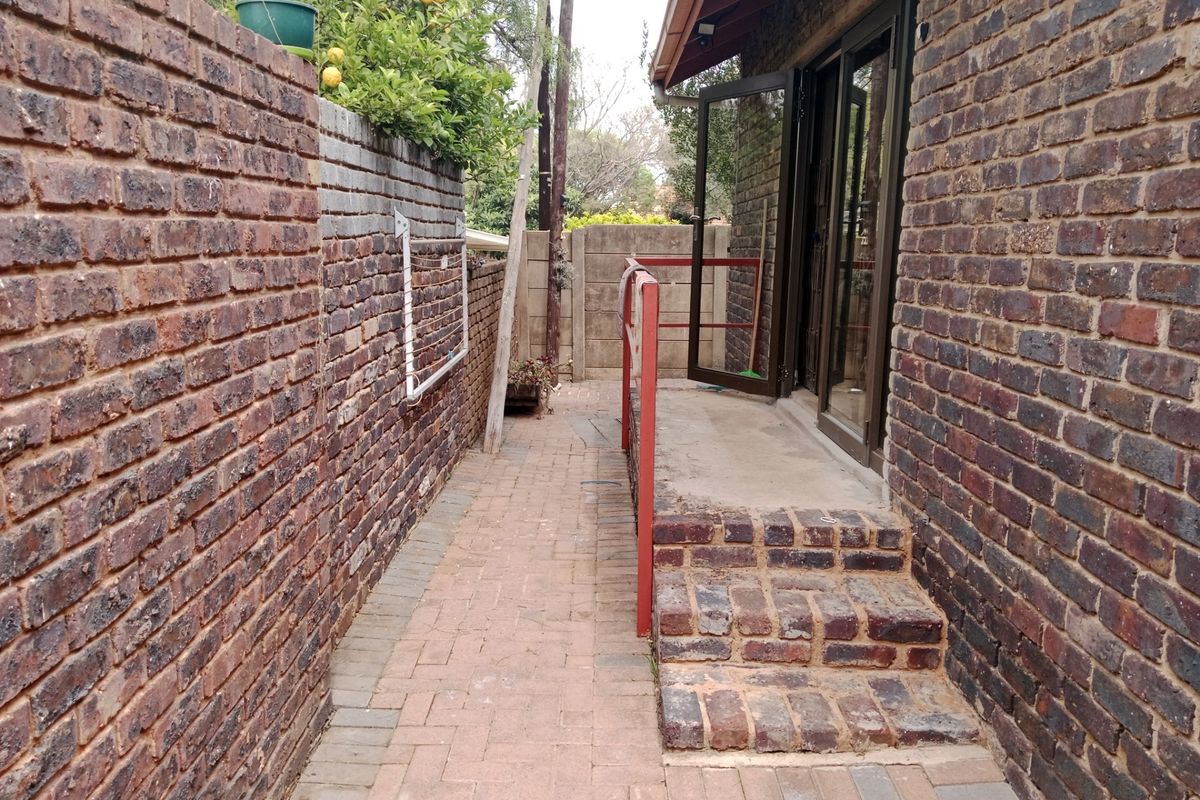 A narrow rear exterior walkway featuring brick boundary walls, paved flooring, and access to the apartment via sliding glass doors with brick steps.