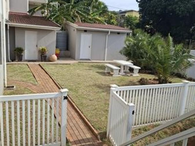 A well-maintained rear garden area featuring a brick paved pathway, white picket fencing, and access to external storage units.