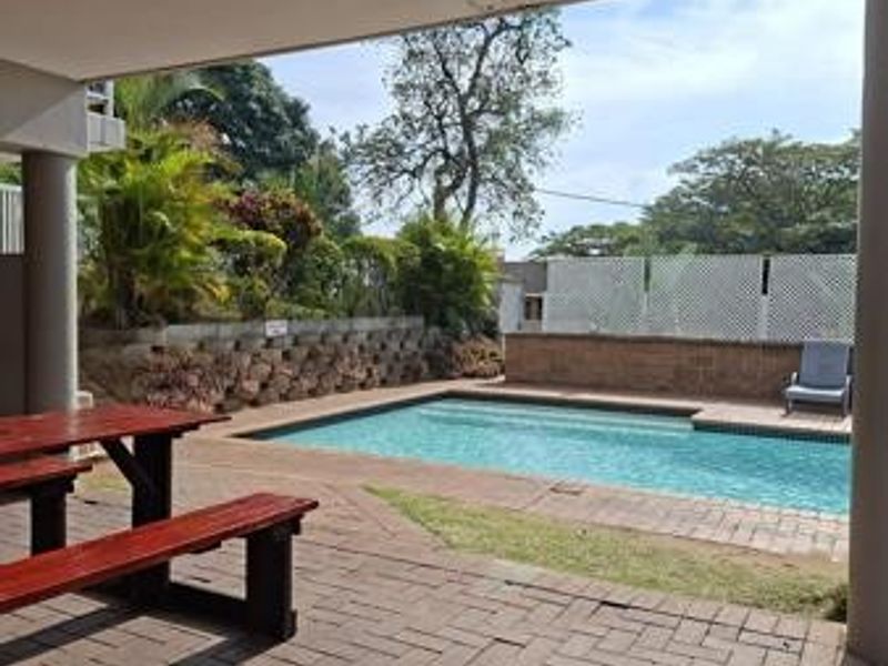 A covered patio area overlooking a private swimming pool with brick paving and a landscaped retaining wall.