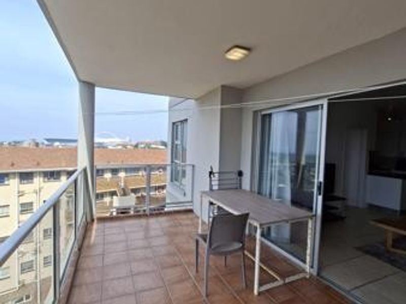 A spacious covered balcony featuring tiled flooring, a modern glass balustrade, and direct access to the interior living area through sliding glass doors.
