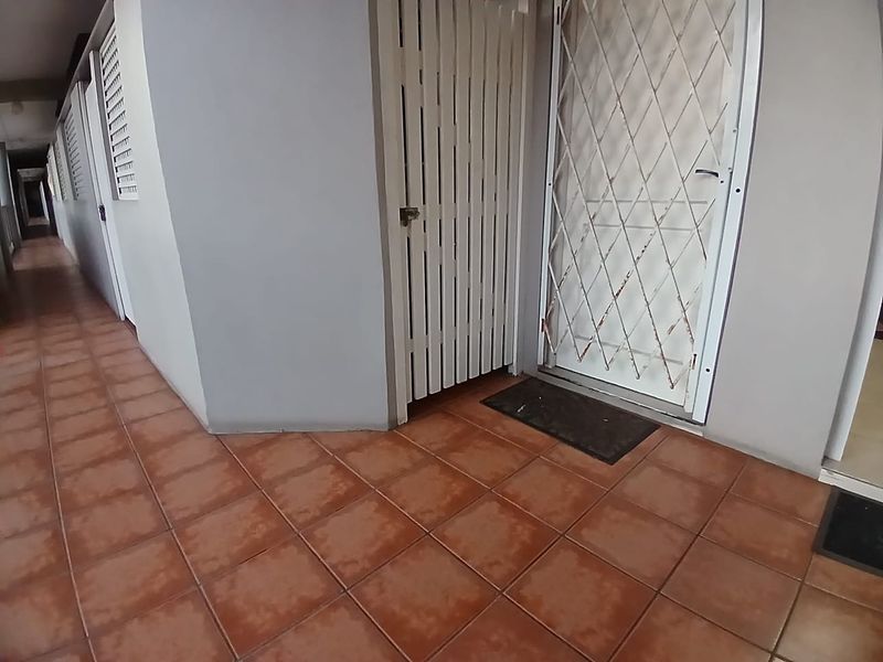 A tiled apartment hallway featuring white security gates and louvered window shutters, providing access to residential units.