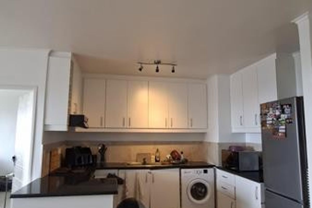 A functional kitchen featuring white cabinetry, dark stone countertops, tiled flooring, and integrated appliances including a built-in oven and hob.