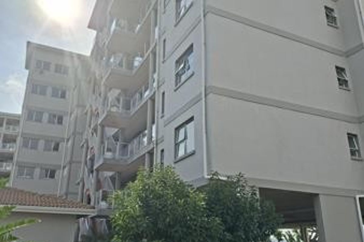 A view of the multi-story apartment building facade featuring balconies with glass balustrades and an undercover parking area at the base.