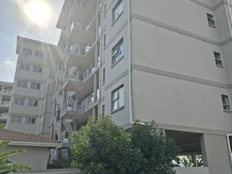 A view of the multi-story apartment building facade featuring balconies with glass balustrades and an undercover parking area at the base.