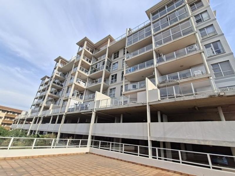 A low-angle view of a modern apartment building featuring multiple levels of balconies with glass balustrades and a spacious tiled terrace area.
