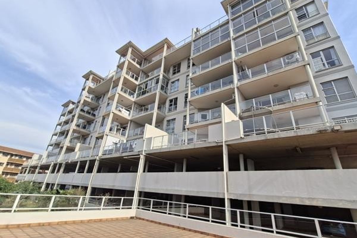 A low-angle view of a modern apartment building featuring multiple levels of balconies with glass balustrades and a spacious tiled terrace area.