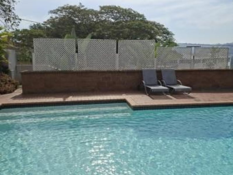 Outdoor swimming pool area featuring brick paving, a low brick retaining wall, and white lattice privacy screening.