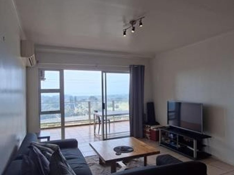 A living room featuring tiled flooring, track lighting, and a sliding glass door that opens onto a balcony with scenic views.