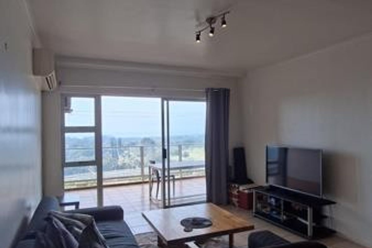 A living room featuring tiled flooring, track lighting, and a sliding glass door that opens onto a balcony with scenic views.