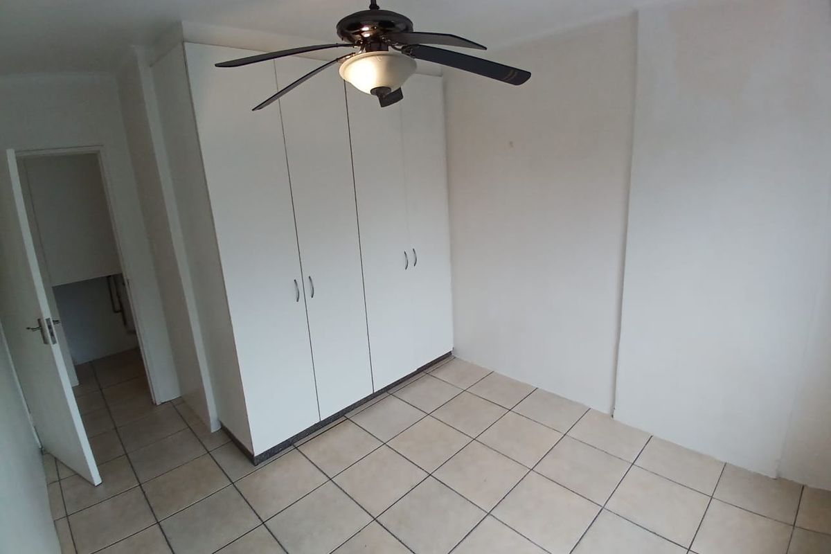A clean, empty bedroom featuring neutral tiled flooring, built-in cupboards, and a ceiling fan, offering a blank canvas for personalization.