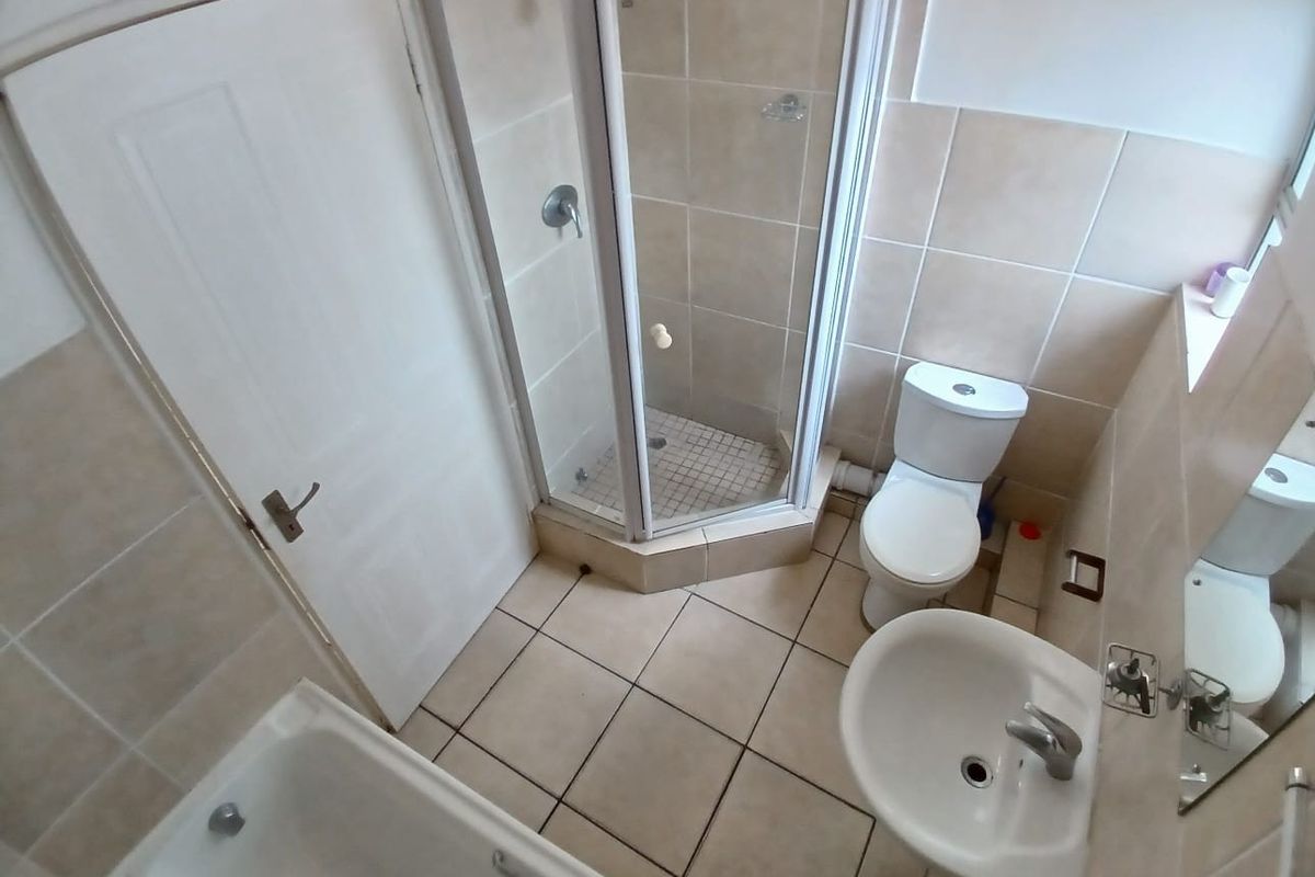 A functional bathroom featuring a separate shower enclosure, bathtub, pedestal basin, and toilet with neutral wall and floor tiling.