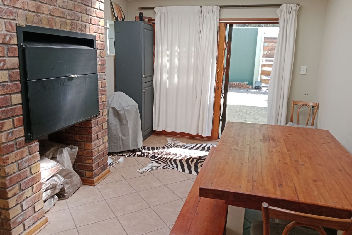 Living area featuring a prominent brick fireplace with built-in braai, tiled flooring, and sliding door access to the outdoor patio area.