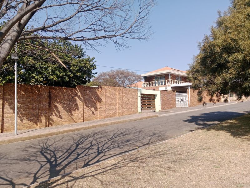 Street view of the property featuring a brick boundary wall, gated entrance, and a two-story residential building with a balcony.