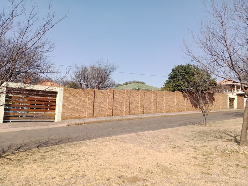 Street view of the property featuring a long brick boundary wall, secure timber slat gate, and integrated electric fencing.