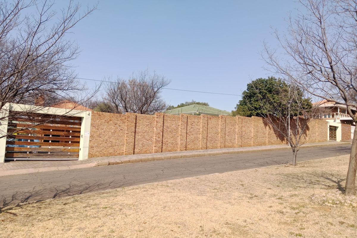 Street view of the property featuring a long brick boundary wall, secure timber slat gate, and integrated electric fencing.
