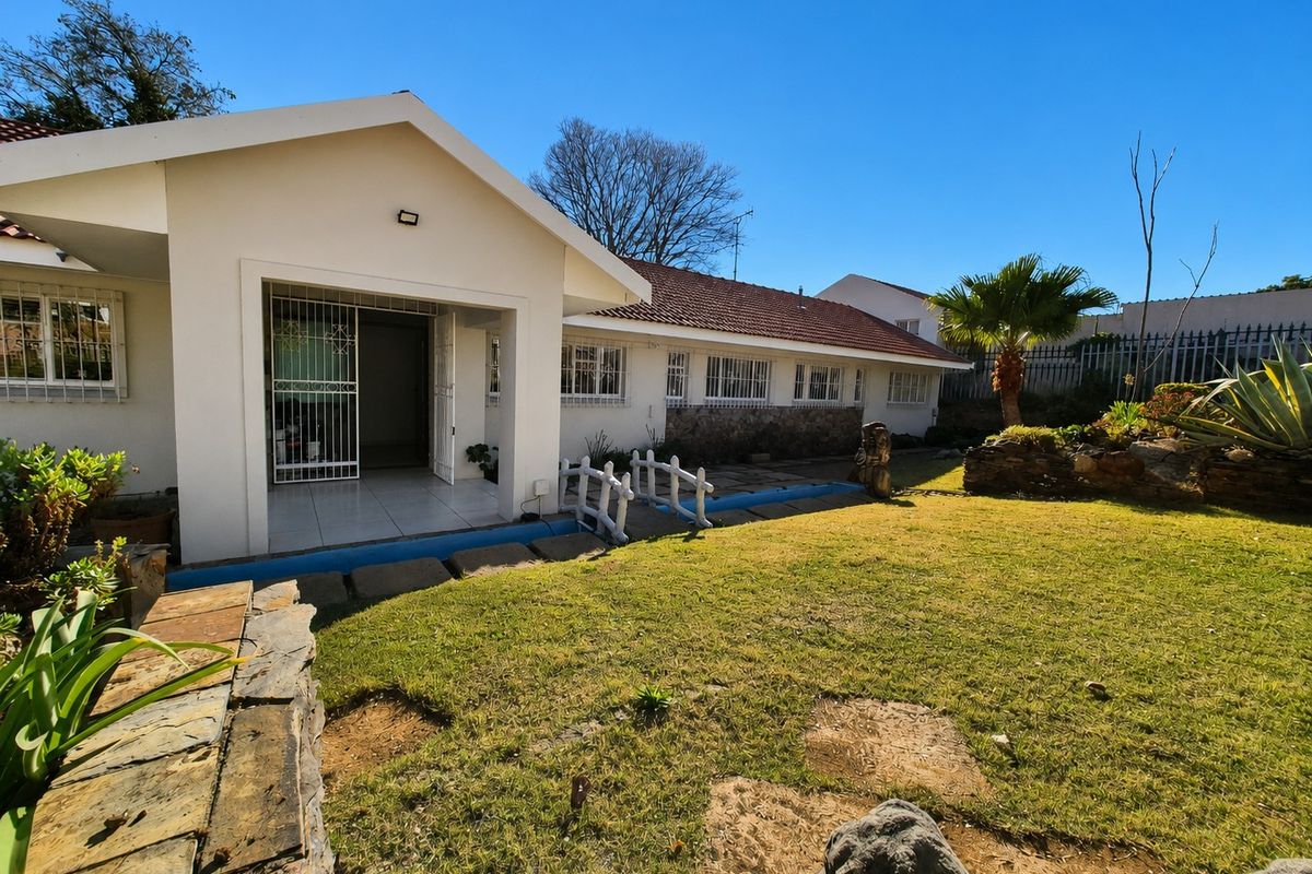 Rear view of the house featuring a covered patio, stone-clad accents, tiled roof, and a landscaped garden with a paved walkway.
