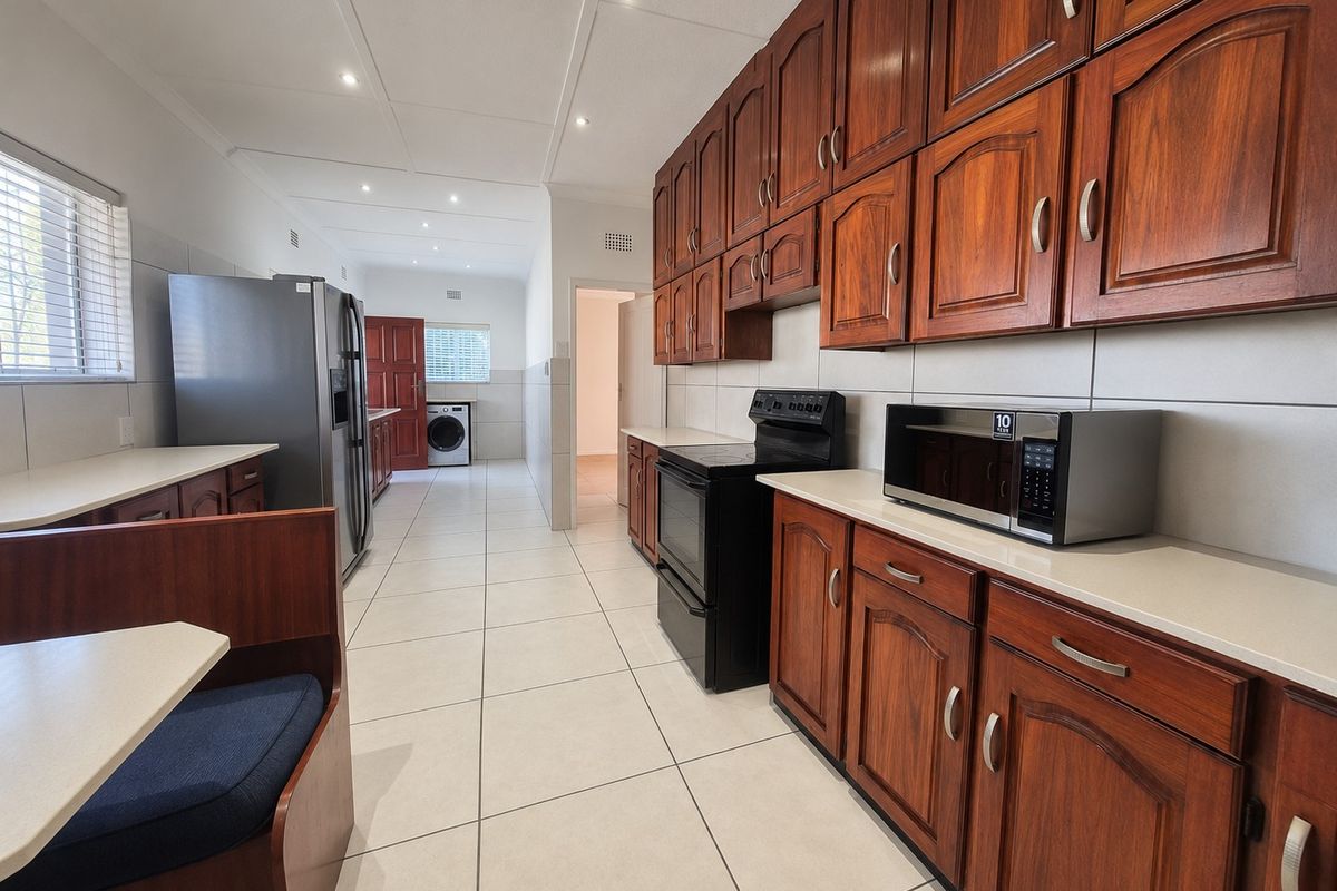 Spacious kitchen featuring traditional wooden cabinetry, tiled flooring, and integrated appliances, offering a functional layout with ample storage and counter space.