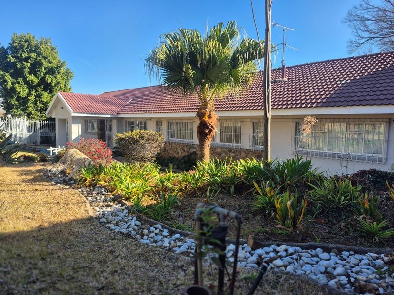 Front elevation of a single-story house featuring a tiled roof, stone cladding accents, and established garden landscaping with security bars on windows.