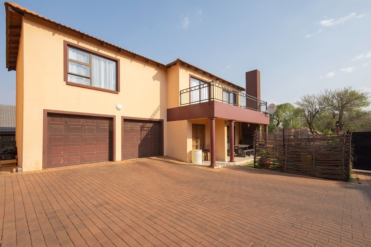 Front elevation of a two-story house featuring a paved driveway, double garage, and an upper-level balcony with a prominent external chimney.