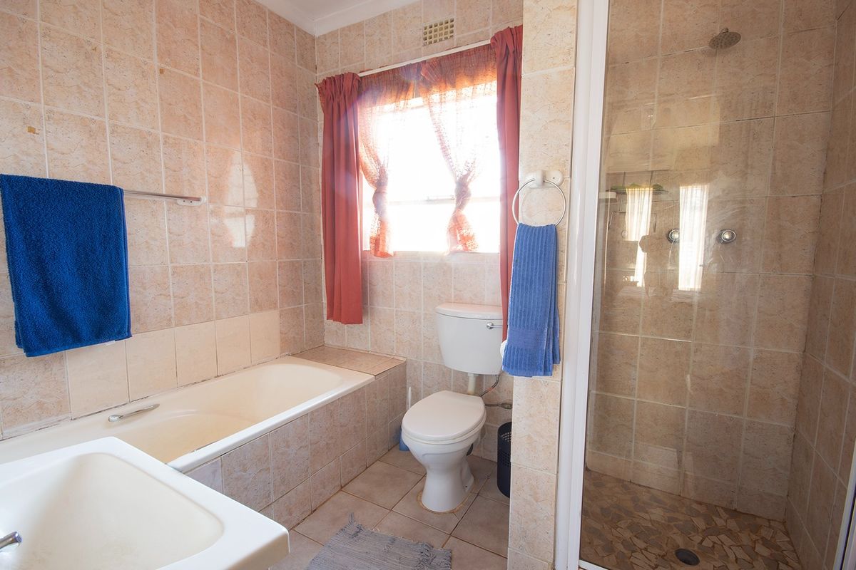 A functional bathroom featuring a built-in bathtub, separate shower enclosure, and toilet, finished with neutral wall and floor tiling.