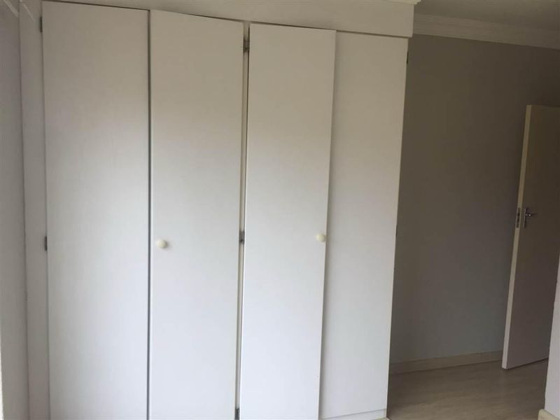 A clean, empty bedroom featuring neutral walls, laminate flooring, and white built-in cupboards with simple hardware.