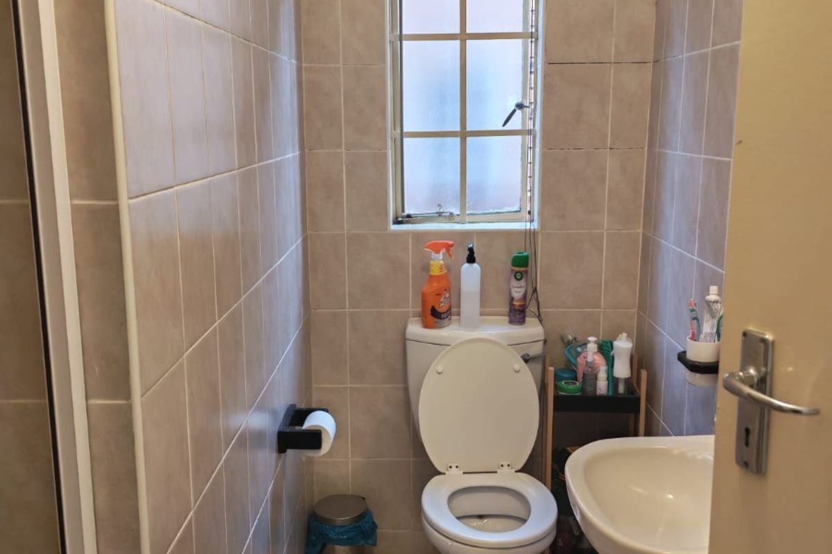 A compact bathroom featuring tiled walls and flooring, a standard toilet, and a pedestal basin with a window for natural light.