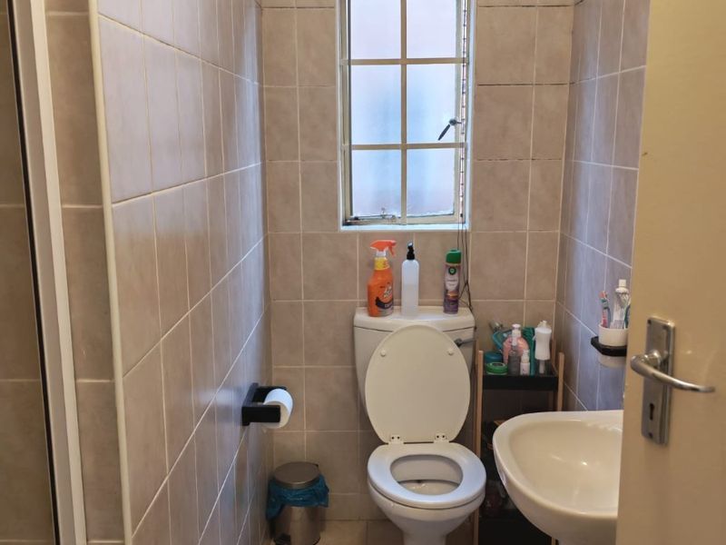 A compact bathroom featuring tiled walls and flooring, a standard toilet, and a pedestal basin with a window for natural light.