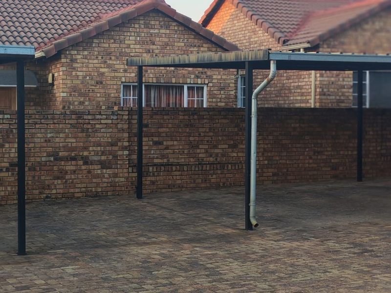 A paved driveway area featuring a functional carport structure with brick boundary walls and traditional tiled roofing.
