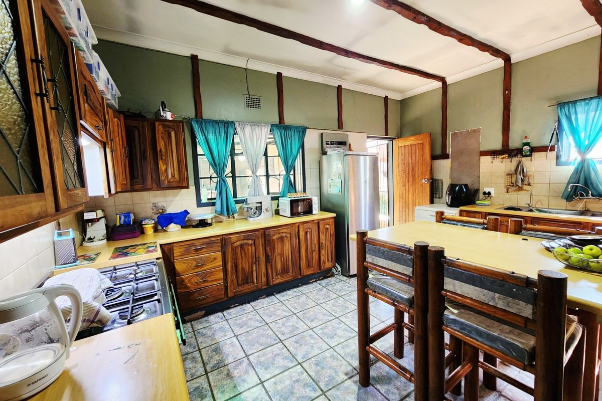 A rustic-style kitchen featuring wooden cabinetry, exposed ceiling beams, tiled flooring, and a gas hob, offering a functional layout with potential for modernization.
