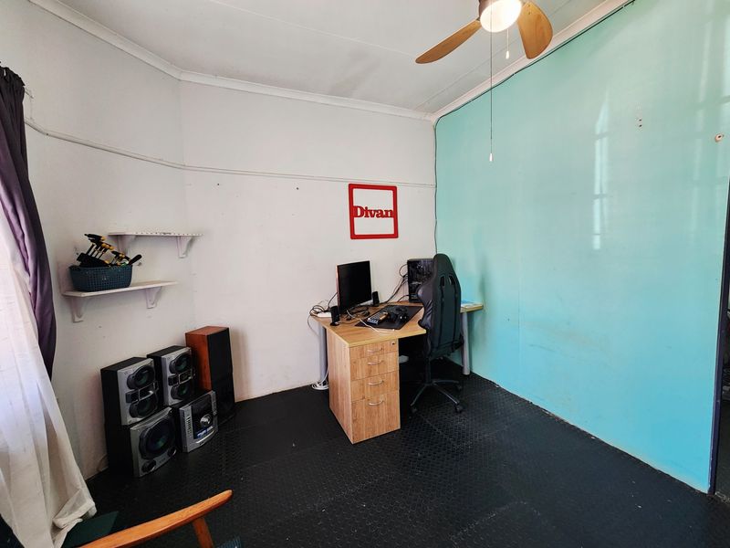 A functional home office space featuring a ceiling fan and wall-mounted shelving, currently utilized as a workspace.
