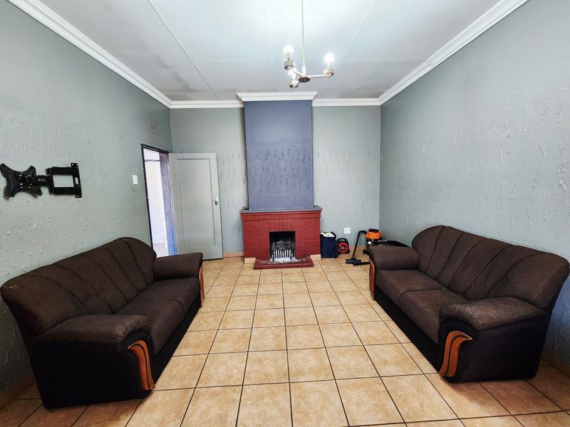 Living room featuring a brick fireplace, ceramic tiled flooring, and decorative ceiling cornice, requiring some cosmetic updates to the walls and ceiling.