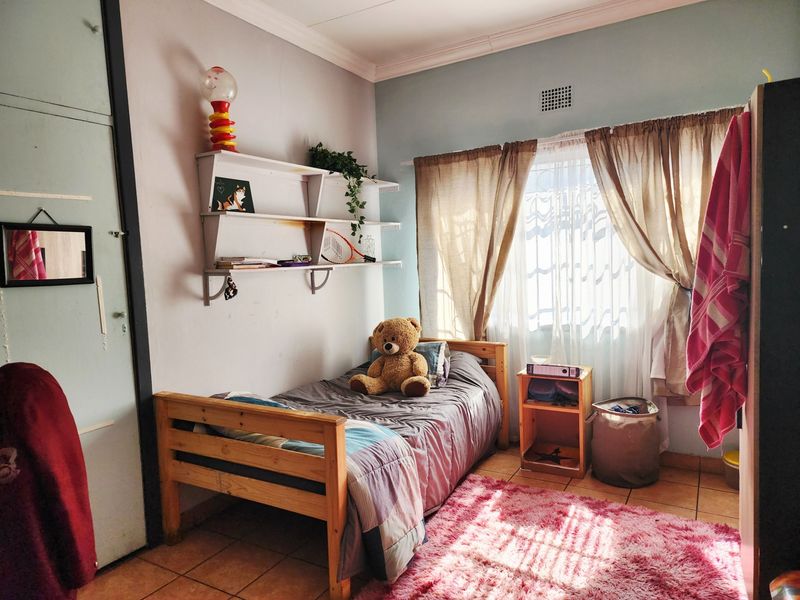 A functional bedroom featuring tiled flooring, built-in cupboard storage, and natural light through a window with curtain treatments.